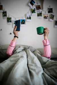 Person Lying Flat Under A Duvet With Phone And Mug